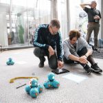 To voksne på gulv, der programerer små blå robotter sammensat af kugler