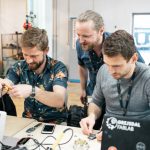 tre mænd ved bord og bærbarcomputer, prøver at konstruerer noget elektronisk