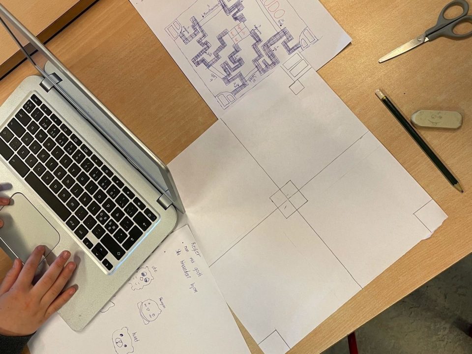 Elev arbejder ved computer; har skitser til design af eget spil liggende på bordet