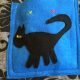 Taske med blå lomme med sort kat, der har dioder som øjne. Et grønt og et rødt kryds er syet og markerer, hvor der kan tændes og slukkes for dioderne